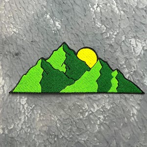 May include: Embroidered patch depicting a mountain range with a yellow sun setting behind the peaks. The mountains are various shades of green, with a black border. The patch is rectangular and designed for application to fabric.