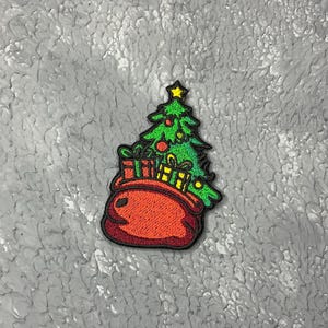 May include: A red felt stocking with a green Christmas tree and presents inside. The stocking has a white trim and a star on top of the tree.