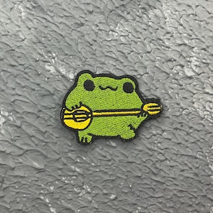 Peut inclure: Un patch brodé représentant une grenouille verte jouant du banjo jaune.