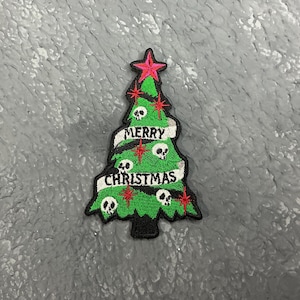 Peut inclure: Patch de Noël en forme de sapin vert avec une étoile rouge au sommet et des crânes sur les branches. Le texte "Merry Christmas" est écrit en blanc sur l'arbre.