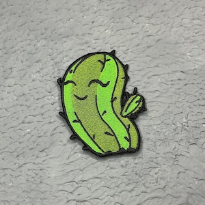 May include: Green and yellow cartoon cactus with a smiling face and a small cactus bud on the side.