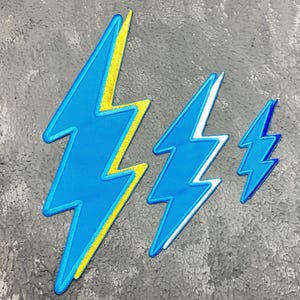 May include: Three lightning bolt shaped patches in different sizes. The largest patch is blue with a yellow outline. The medium patch is blue with a white outline. The smallest patch is blue with a white outline.