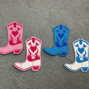 May include: Four embroidered iron-on patches in the shape of cowboy boots. The boots are pink, white, blue, and white with blue accents. Each boot has a heart with flames on the front.