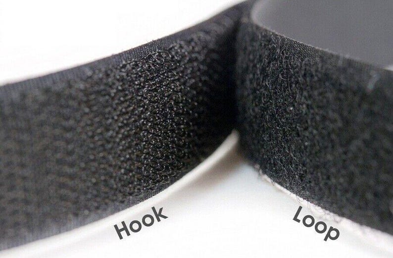 Op de afbeelding: Close-up van zwarte klittenbandstrips. De afbeelding toont de getextureerde oppervlakken van de haak- en luskanten, met de woorden "Hook" en "Loop" gedrukt op de witte achterkant.
