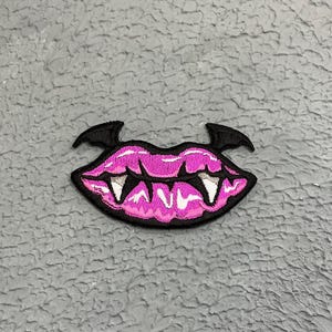 May include: Pink and black embroidered patch of a vampire mouth with fangs.