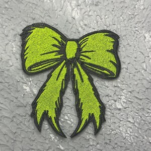 May include: A lime green embroidered bow with black stitching. The bow is a decorative patch.