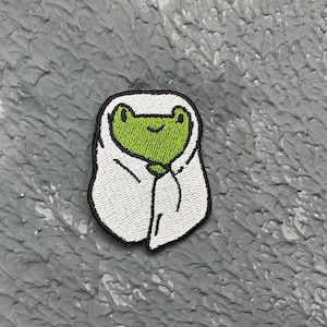 May include: Green frog wearing a white hooded robe, embroidered patch.