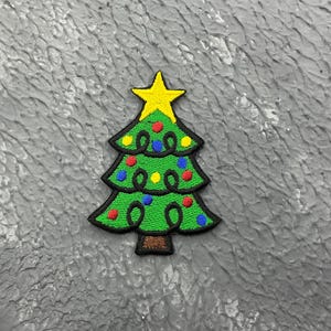 May include: A green felt Christmas tree with a yellow star on top and colourful ornaments. The tree is outlined in black and has a brown trunk.