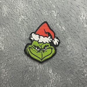 May include: Green Grinch character wearing a red and white Santa hat. The Grinch is embroidered on a fabric patch.