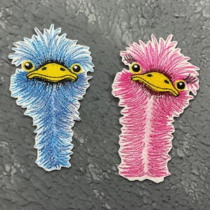 May include: Two embroidered iron-on patches of ostriches. One ostrich is blue with a yellow beak and the other is pink with a yellow beak.