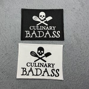 May include: Two black and white embroidered patches with a skull and crossbones design. The patches say "Culinary Badass" in white text.