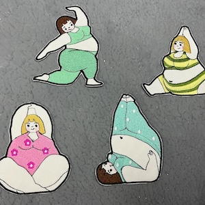 May include: Four embroidered iron-on patches featuring different women in various poses. The patches are white with colorful details. The women are wearing different outfits, including a green and white outfit, a yellow and white striped outfit, a blue and white polka dot outfit, and a pink and white outfit.