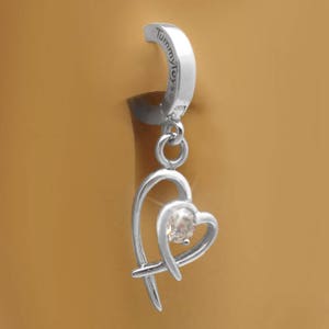 Puede incluir: Anillo de ombligo plateado con un colgante de coraz&oacute;n que cuelga con un cristal transparente. El anillo est&aacute; grabado con las palabras "Tummy Toys".