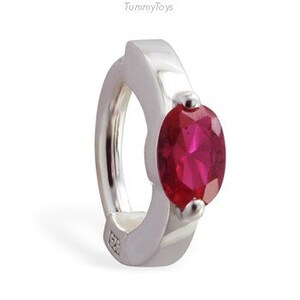 May include: A silver ring with a red oval-shaped gemstone. The ring is a clicker style, meaning it opens and closes with a click.
