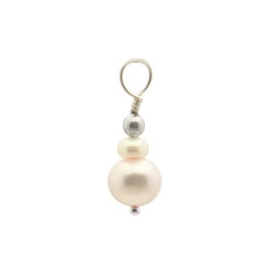 May include: A silver charm with three pearls. The largest pearl is a light pink color, the middle pearl is white, and the smallest pearl is silver.