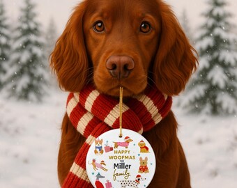 May include: A red-haired dog wearing a red and white striped scarf, holding a round Christmas ornament. The ornament features dog illustrations and the text "HAPPY WOOFMAS The Miller Family 2025". The background shows a snowy winter scene with evergreen trees.