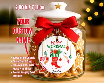 May include: A white ceramic Christmas ornament with the text "MERRY WORKMAS" and festive illustrations, hanging in front of a jar filled with gingerbread cookies. The ornament is 2.80 inches (7.11 cm) in diameter and has a red bow.