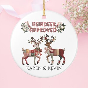 Könnte beinhalten: Weißer Keramik-Weihnachtsschmuck mit zwei Rentieren mit gemusterten Körpern und Schleifen. Der Text "REINDEER APPROVED" steht oben, mit "KAREN & KEVIN" unten. Er hat eine goldene Schnur zum Aufhängen.