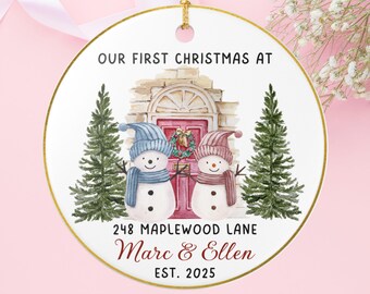 May include: A circular Christmas decoration with a gold edge and hanging loop. It depicts two snowmen wearing hats and scarves, standing before a house. Text on the ornament reads "OUR FIRST CHRISTMAS AT 248 MAPLEWOOD LANE Marc & Ellen EST. 2025."