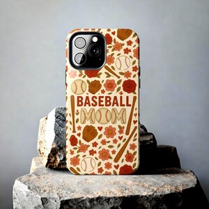 Könnte beinhalten: Beige Handyhülle mit Baseball-Motiv. Sie zeigt Basebälle, Handschuhe, Schläger und Blumen in Braun-, Rot- und Pfirsichtönen. Der Text "BASEBALL MOM" ist auf der Hülle zu sehen.