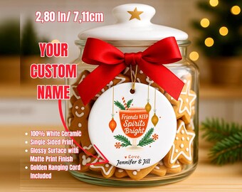 May include: A white ceramic Christmas ornament, 2.80 inches (7.11 cm) in diameter, with a red bow. The ornament has the text "Friends Keep Spirits Bright" and is hanging in front of a jar of gingerbread cookies.