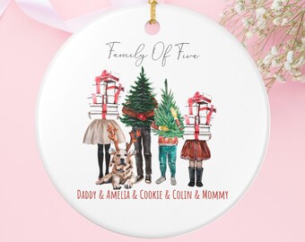 Peut inclure: Ornement de Noël en céramique blanche avec une ficelle dorée. L'ornement présente une illustration familiale avec un chien, des cadeaux et des arbres de Noël. Le texte indique "Family Of Five" et des noms.