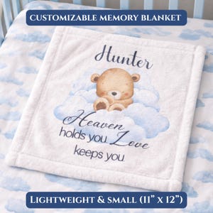 Könnte beinhalten: Weißes Babydecke mit einer Teddybär-Illustration auf einer Wolke. Auf der Decke steht der Name "Hunter" und der Text "Heaven holds you. Love keeps you." Die Decke ist leicht und klein, mit den Maßen 28 cm x 30 cm.