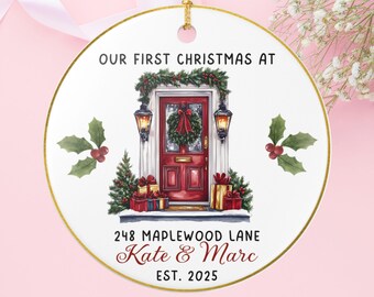 May include: A circular Christmas ornament with a gold edge and hanging string. It depicts a red front door with festive decorations and gifts. Text includes "OUR FIRST CHRISTMAS AT", address details, and "Kate & Marc EST. 2025".