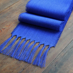 May include: A royal blue table runner with a fringe border. The runner is made of a woven fabric and has a subtle texture.