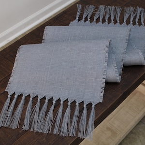 May include: A gray linen table runner with a fringed edge. The runner is approximately 14 inches wide and 72 inches long.