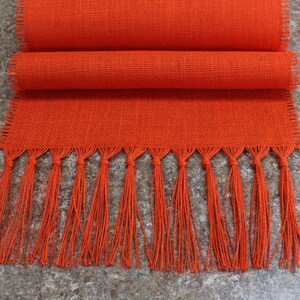 May include: Orange burlap table runner with fringe. The runner is folded in half and has a woven texture.