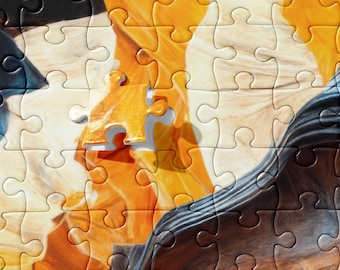 Könnte beinhalten: Eine Nahaufnahme eines Puzzles mit einem fehlenden Teil. Das Puzzle zeigt ein farbenfrohes abstraktes Design in Orange, Weiß und Schwarz. Das fehlende Teil ist ein kleines, goldfarbenes Teil.