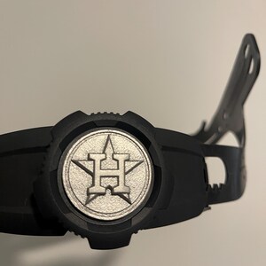 Może przedstawiać: Czarny kask do uderzania w baseball z srebrnym logo Houston Astros.