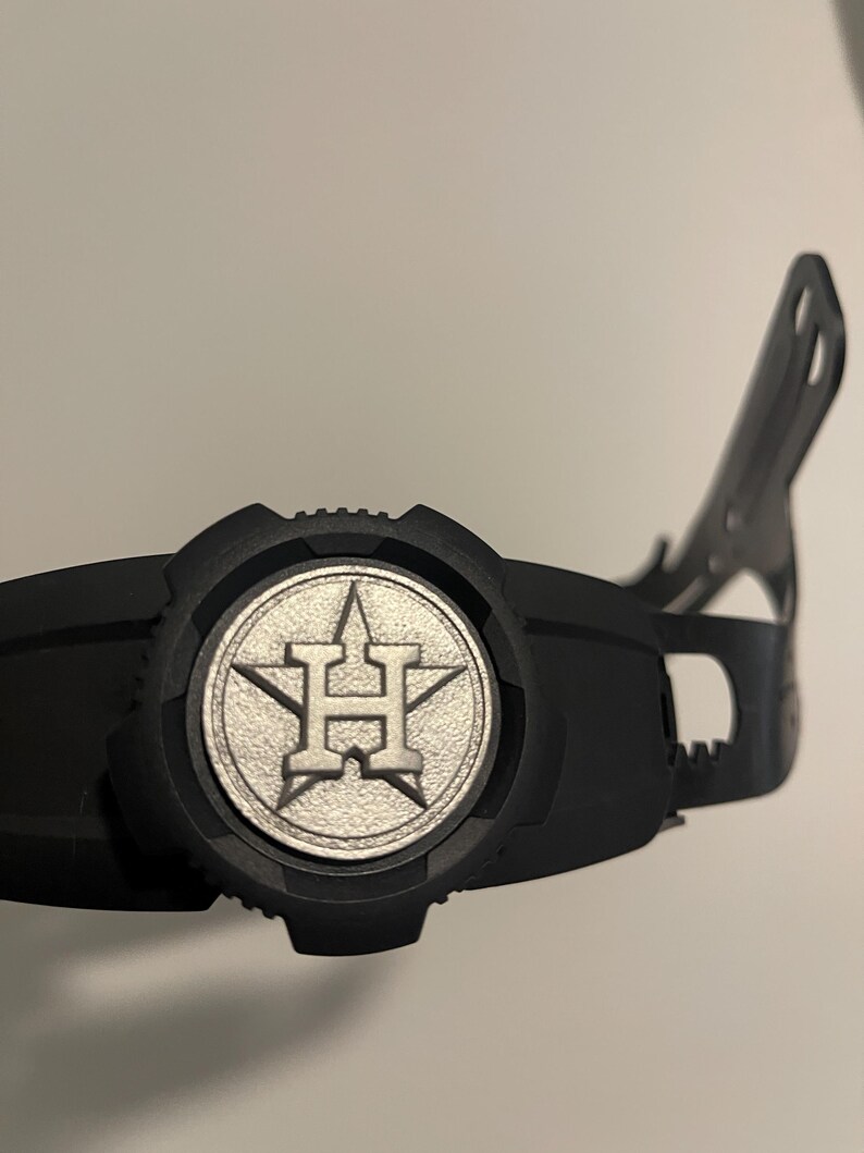 Może przedstawiać: Czarny kask do uderzania w baseball z srebrnym logo Houston Astros.