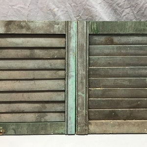 May include: A pair of weathered green wooden shutters with a metal latch on the right side. The shutters are closed and have horizontal slats.