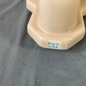 May include: Close-up of the bottom of a pink ceramic toilet bowl with the text "K.O.K. USA" in blue.