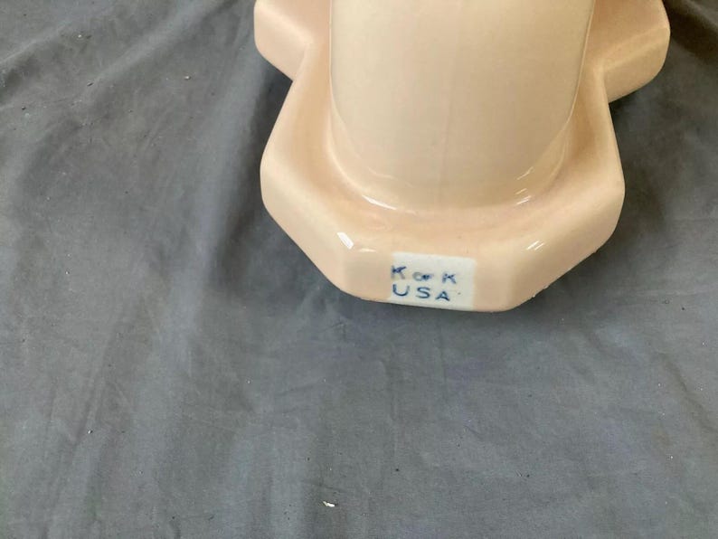 May include: Close-up of the bottom of a pink ceramic toilet bowl with the text "K.O.K. USA" in blue.