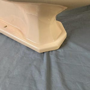 May include: The bottom of a white porcelain pedestal sink with a rounded, octagonal base.