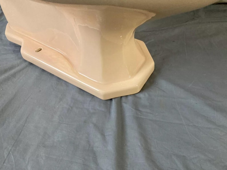 May include: The bottom of a white porcelain pedestal sink with a rounded, octagonal base.