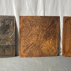 May include: Three antique tin ceiling tiles with intricate designs. The tiles are square and have a distressed, rusty look. The designs are in a floral pattern.