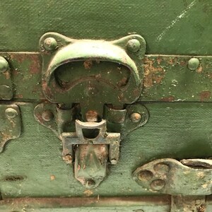 May include: Close-up of a green metal latch with a handle and a metal clasp. The latch is attached to a wooden box.