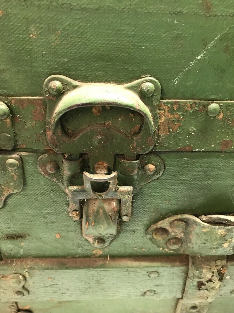May include: Close-up of a green metal latch with a handle and a metal clasp. The latch is attached to a wooden box.
