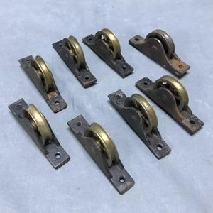 May include: Eight antique brass and black metal window sash pulleys. Each pulley has a small brass wheel with a groove for a rope or cord.