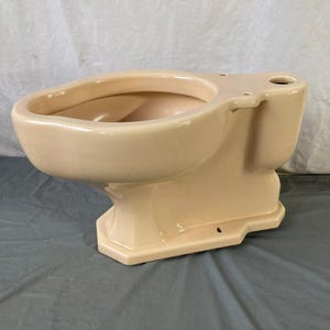 May include: A beige ceramic toilet bowl with a rounded front and a rectangular base. The toilet bowl is missing the seat and lid.