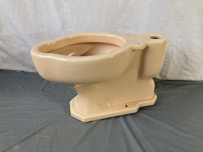 May include: A beige ceramic toilet bowl with a rounded front and a rectangular base. The toilet bowl is missing the seat and lid.