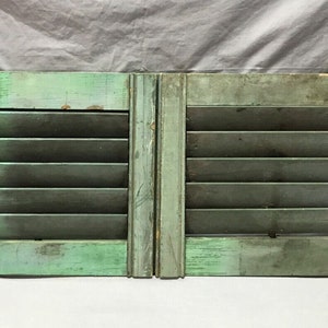 May include: A pair of antique wooden shutters painted in a faded green color. The shutters have multiple louvers and are attached with metal hinges. Each shutter has a decorative metal latch.