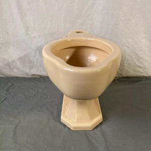 May include: A cream-colored ceramic toilet bowl with a pedestal base. The bowl has a rounded shape and a smooth, glossy finish.
