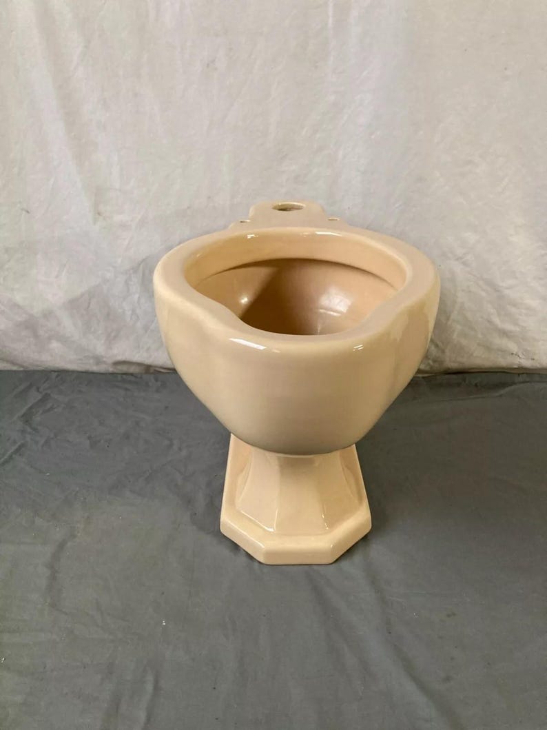 May include: A cream-colored ceramic toilet bowl with a pedestal base. The bowl has a rounded shape and a smooth, glossy finish.