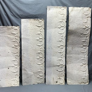 May include: Four antique tin ceiling tiles with a white painted finish and a repeating floral design. The tiles are slightly warped and show signs of age.
