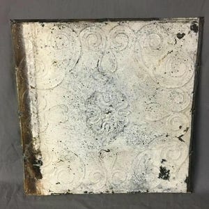 May include: A white ceramic tile with a raised embossed design of swirling patterns. The tile has a distressed, aged look with some areas of discoloration.
